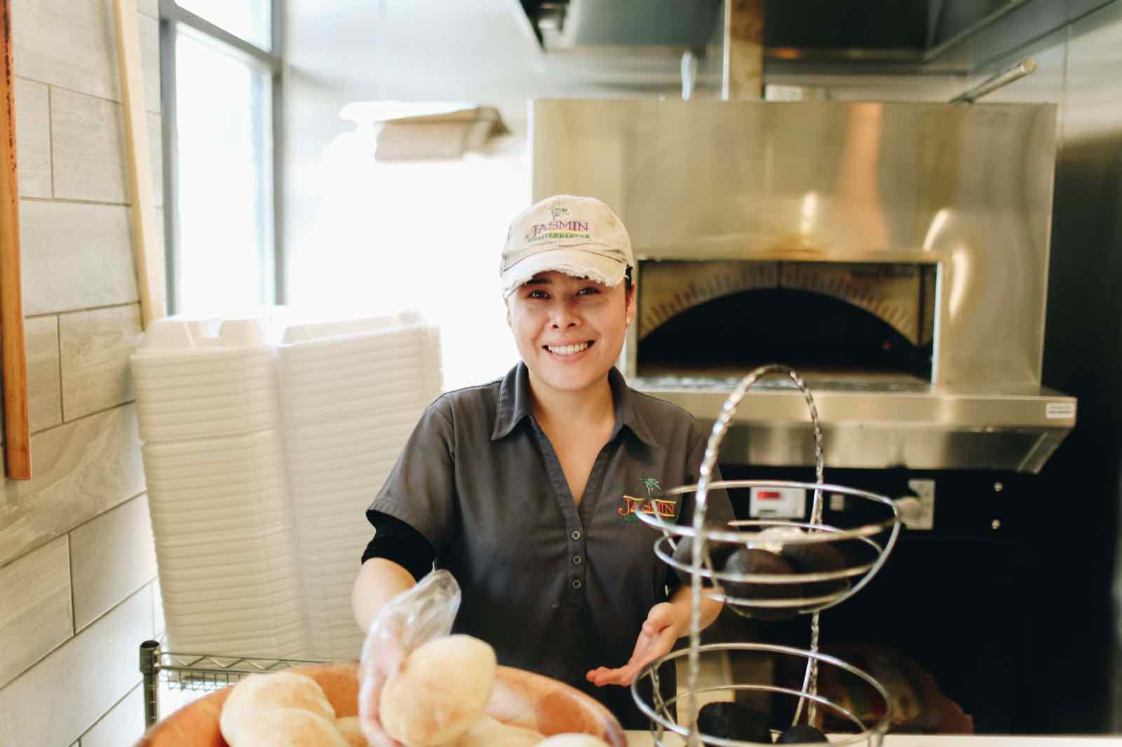 Smiling Jasmin team member serving fresh pita in front of the oven